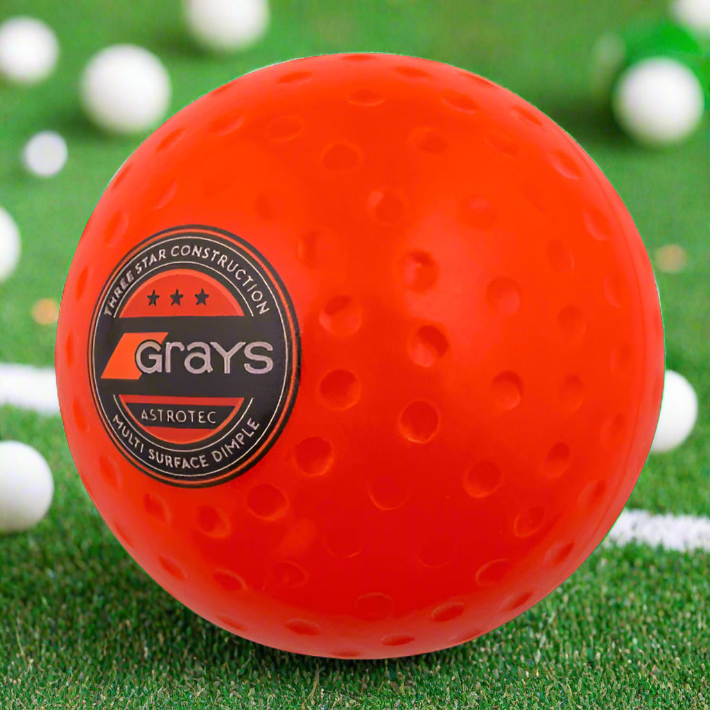 An orange Grays AstroTec field hockey ball with the brand logo visible on it.