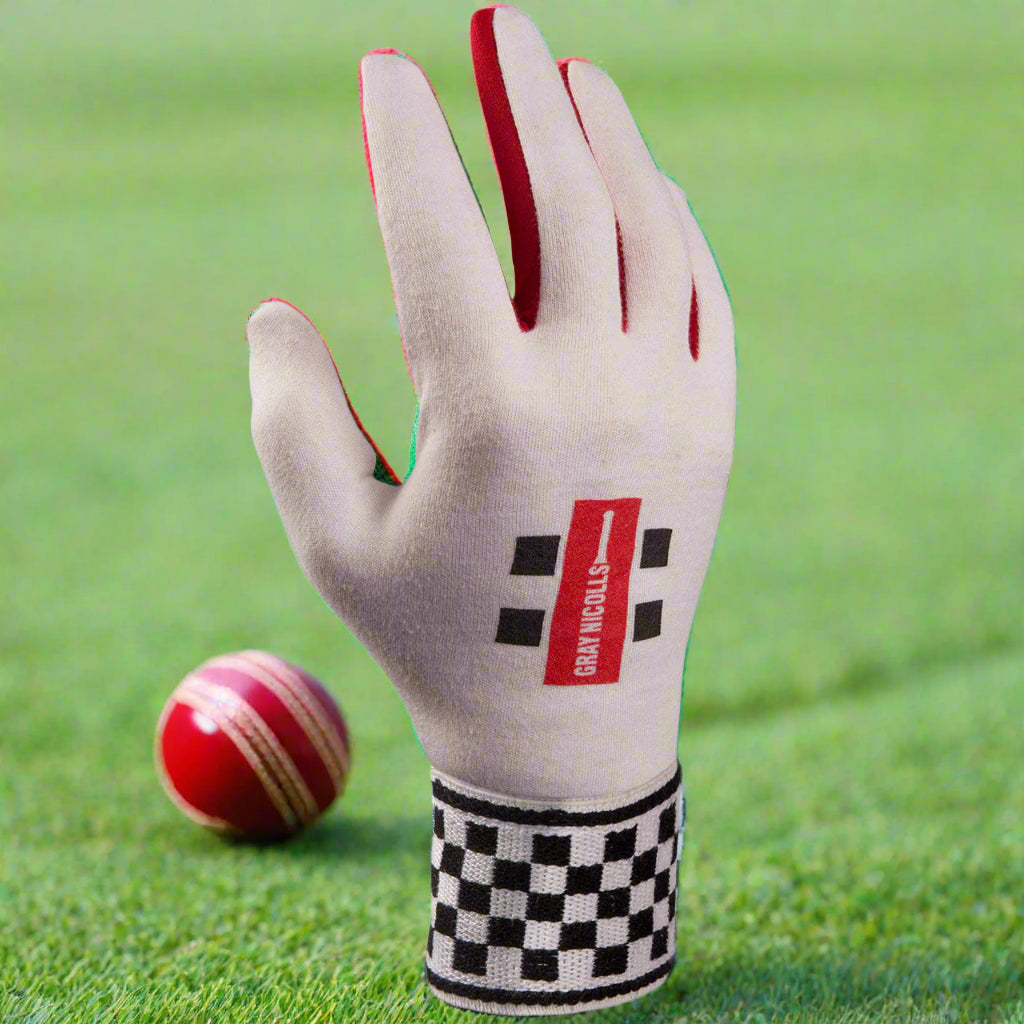 A cricket wicketkeeping glove featuring a chamois palm and a checkered pattern on the wrist strap, predominantly white with gray and red accents.