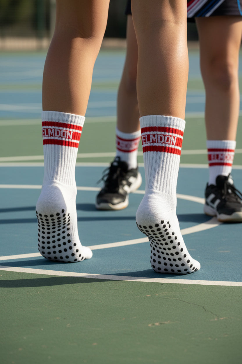 A pair of white sport socks with red and white striped cuffs, word 'ELMDON' in white, and the other with black grip dots.