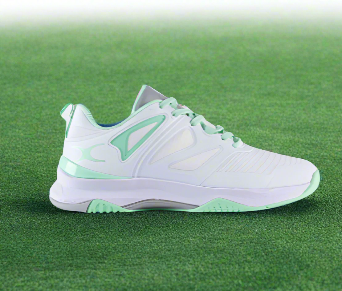 A pair of Gilbert Impact Netball Shoes, predominantly white with green accents, designed for court play with cushioned soles and supportive upper structure.