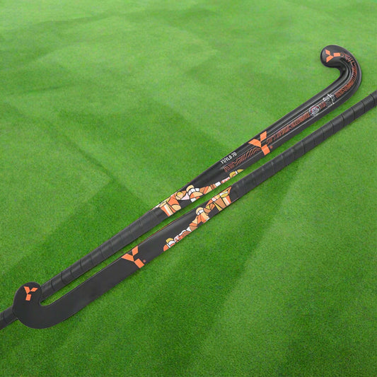 A black field hockey stick with a low bow, featuring orange accents and decorative patterns, including what appears to be a stylized cat wearing a hat.