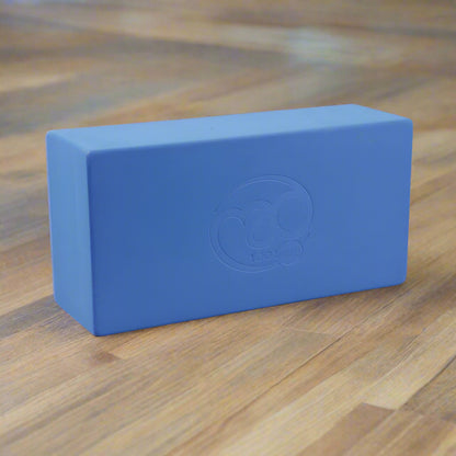A blue, high-density yoga block with a non-slip surface and a logo embossed on the front.