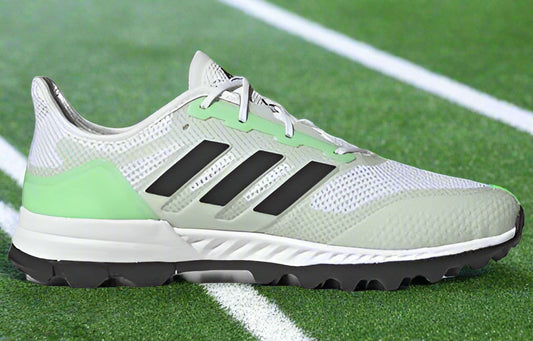 A pair of white adidas hockey shoes with blackstripes, showcasing the sole with rubber traction patterns.